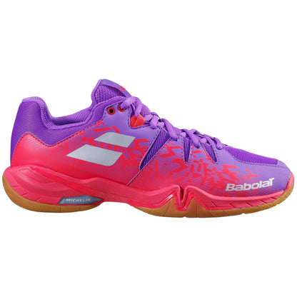 The Babolat Shadow Spirit Women's Badminton Shoes in Dewberry and Fiery Red boast a dynamic purple upper accented with pink and red details. Silver logo highlights stand out on the shoe, while a brown and red Michelin rubber sole ensures superior grip. The "Babolat" brand name is prominently displayed on the side.