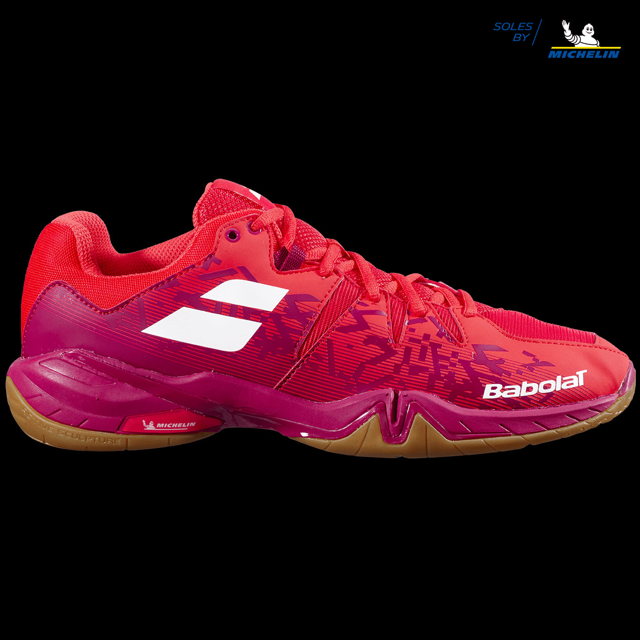 A Babolat Shadow Spirit men's badminton shoe in Cherry Tomato, showcasing dynamic patterns and a white logo, is set against a sleek black background. The gripsole is expertly crafted from Michelin rubber.