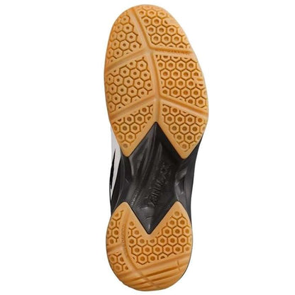 The image showcases the sole of a Yonex Power Cushion 36 men's badminton shoe, presenting a honeycomb pattern in light brown. The sole, designed with hexagonal and triangular shapes for improved traction, perfectly complements the black upper accented with blue, emphasizing its Ergoshape design for enhanced performance.