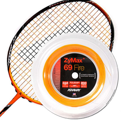 A badminton racket is displayed alongside a reel of Ashaway ZyMax 69 Fire Badminton String. The vibrant orange string, neatly coiled in its transparent packaging, emphasizes impressive durability and extreme tension with the packaging text highlighting its strength and extended string life against a white backdrop.