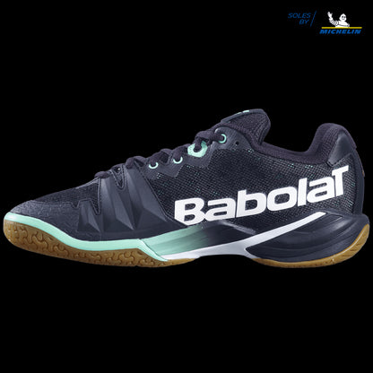 A side view of the Babolat Shadow Tour Badminton Shoes in black and green, featuring "Soles by Michelin" branding. Enhanced with DCS technology, the shoes showcase a textured surface and a brown gum sole designed for dynamic response.