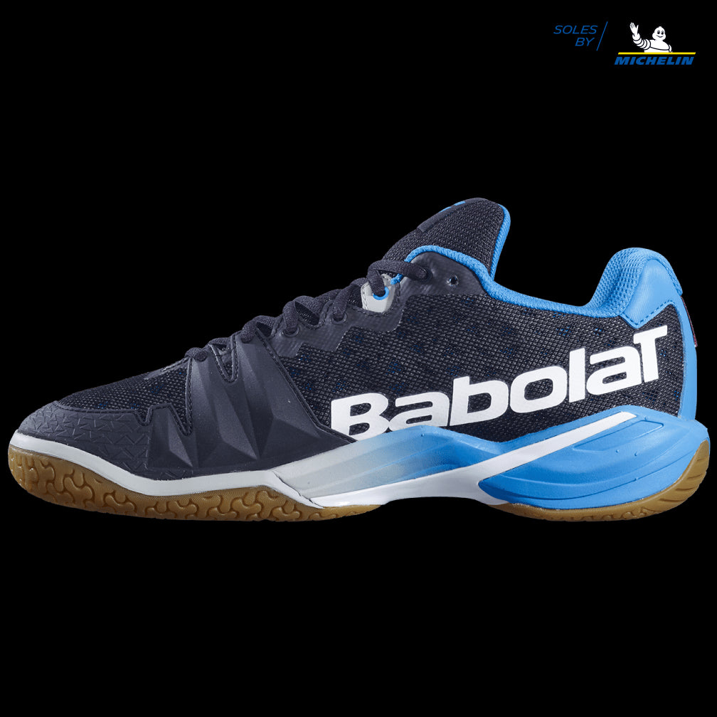 The Babolat Shadow Tour Badminton Shoes in Black Light Blue feature a gum sole with "Soles by Michelin" branding. These shoes are designed with shock absorption for enhanced comfort, and their textured design includes white accents and the iconic Babolat logo on a black background, ensuring excellent dynamic response on the court.