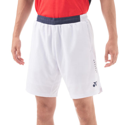 A person in a red shirt and Yonex 15131 Men's Shorts in white, featuring the VERY COOL technology and UV reduction, stands against a plain background. These athletic shorts, with a dark waistband and small logo, provide a comfortable fit suitable for sports or casual wear.