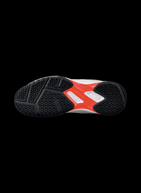 The image showcases the sole of a Yonex Power Cushion 50 badminton shoe against a black backdrop. The predominantly black, textured design ensures grip, complemented by a red section in the center that features a white rectangular label with text, emphasizing its lightweight performance.