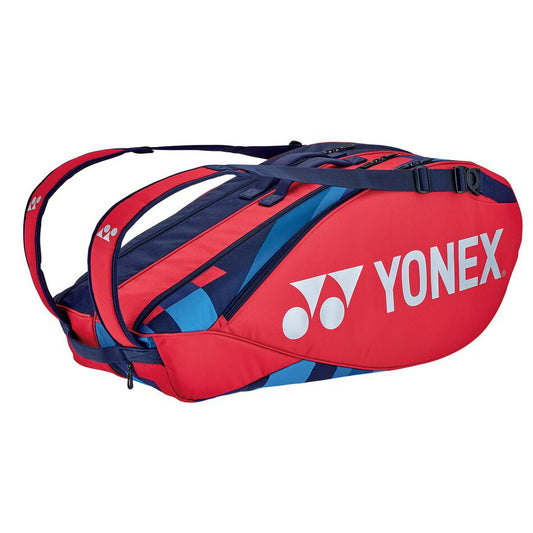 The Yonex 92226EX 6 Piece Pro Racket Bag - Scarlet is crafted with professional-grade quality, featuring a unique red and blue design complete with shoulder straps. The white Yonex logo adds a touch of style, enhancing the bag's function and aesthetics.