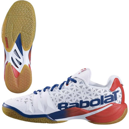 The Babolat Shadow Tour Badminton Shoes in white and blue, developed in collaboration with Michelin, boast red accents and a textured gum sole. The "Babolat" brand name is prominently displayed on the side, along with an image that highlights the DCS technology integrated into the detailed sole design.