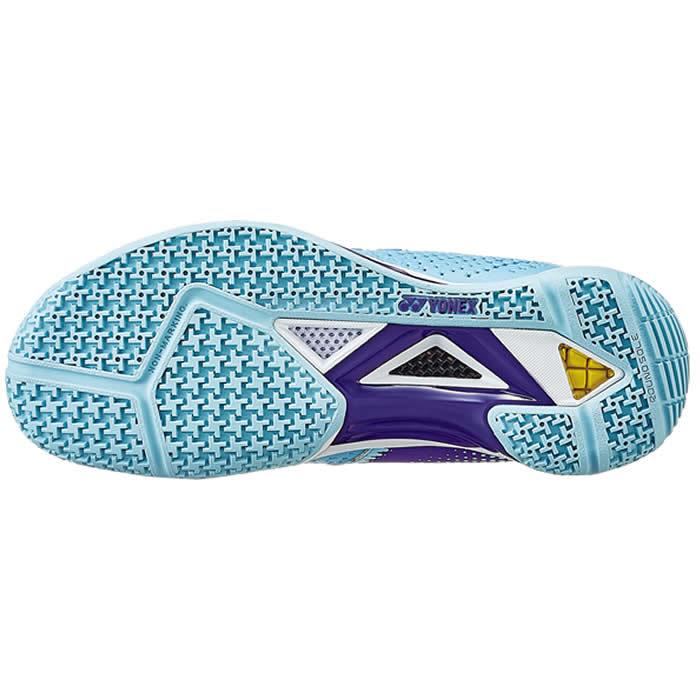 The image displays the sole of the Yonex Power Cushion Eclipsion Z2 Women's Badminton Shoes in light blue. The sole is designed with a textured light blue rubber surface featuring a checkerboard pattern for improved grip, paired with a purple midsole section that incorporates geometric elements and Yonex's Power Cushion technology to offer enhanced stability and cushioning.