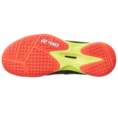 The image highlights the sole of the Yonex Power Cushion Comfort Z3 Mens Badminton Shoes in black, featuring Feather Bounce Foam. Its design is accentuated with red and lime green textured patterns and prominently displays the Yonex logo. The unique tread pattern offers exceptional grip, emphasizing the advanced Yonex Power Cushion technology.