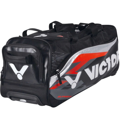 The Victor Multi Sportbag BG9712 Large Travel Badminton Bag is a black and gray duffel bag with red accents, showcasing the "Victor" logo in bold white letters. This versatile piece of travel luggage comes equipped with sturdy wheels, multiple compartments, and a convenient carrying handle for easy transport.