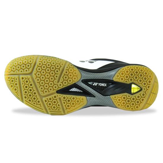 The image highlights the sole of a Yonex Power Cushion 65Z2 Men's Badminton Shoe, featuring a hexagonal tread pattern designed to enhance grip. The sole exhibits a vibrant mix of yellow and gray colors, with the Yonex logo and brand name elegantly presented in white on the side.