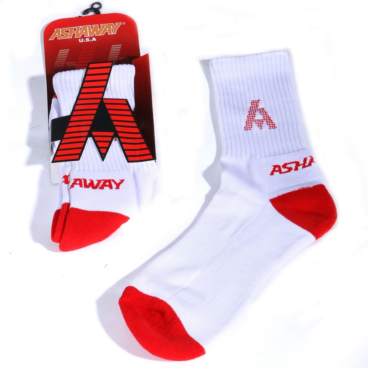 A pair of Ashaway Badminton Socks is shown, ideal for racket sports. The socks are made from white fabric with red accents on the toes and heels. One sock is packaged with a black and red label displaying the "Ashaway U.S.A." brand and logo, while the other lays flat, crafted to reduce blistering.