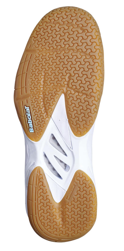 Close-up of the sole of a Babolat Shadow Spirit 2023 women's badminton shoe, featuring a design reminiscent of supportive tennis shoes, with both honeycomb and radial patterns. The tan sole includes a white section in the middle showcasing "Babolat" in blue lettering.