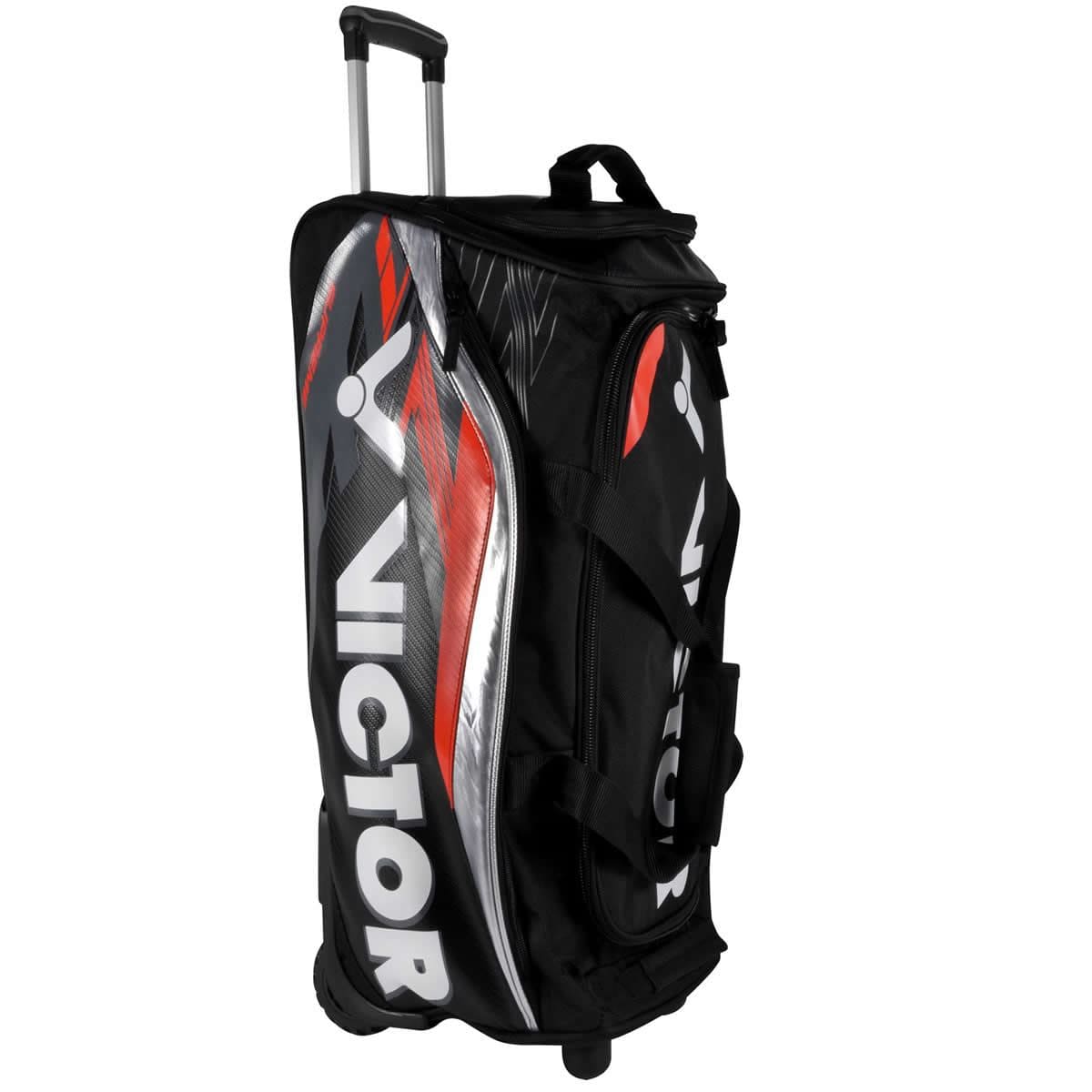 The Victor Multi Sportbag BG9712 Large Travel Badminton Bag is a black rolling sports bag featuring a handle and bold "VICTOR" branding in white letters. The design includes red and gray accents on the side panels. This versatile piece of travel luggage offers sturdy wheels and multiple compartments for added convenience.