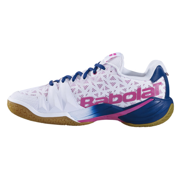 The Babolat Shadow Tour Badminton Shoes in white and pink showcase a white and blue design with pink accents, complete with a gum sole and mesh construction. Enhanced by DCS technology, the shoe prominently features "Babolat" in large pink letters on the side.