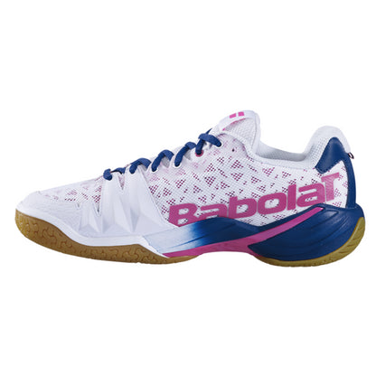 The Babolat Shadow Tour Badminton Shoes in white and pink showcase a white and blue design with pink accents, complete with a gum sole and mesh construction. Enhanced by DCS technology, the shoe prominently features "Babolat" in large pink letters on the side.