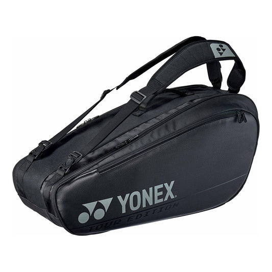 Introducing the Yonex 92026EX Pro 6 Piece Badminton Racket Bag in black, showcasing a sleek design. It features a spacious main compartment that can accommodate up to six rackets and includes an additional shoe compartment. The bag is equipped with an adjustable padded shoulder strap and displays the Yonex logo printed on the side, enhancing its streamlined profile.