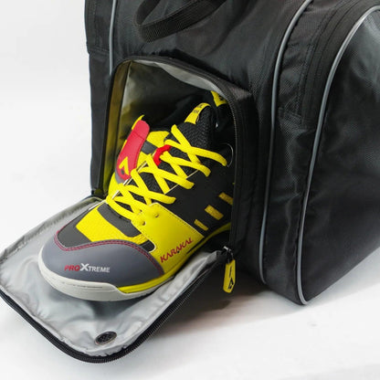 A partially open black sports bag reveals a pair of vibrant sports shoes with bright yellow, black, and red accents. One shoe is labeled "Karakal Pro Xtreme," while the gray interior lining of the bag suggests it might be the Karakal Pro Tour 2.0 Elite Racket Bag by Karakal, ideal for tournament players.