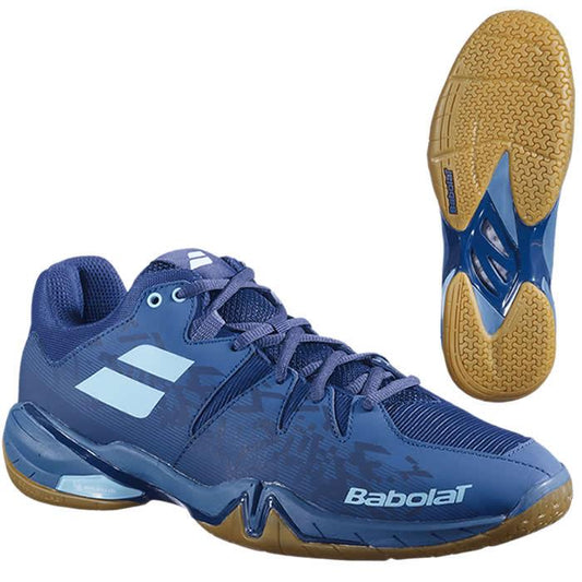 The Babolat Shadow Spirit Badminton Shoes in Dark Blue, by Babolat, are displayed from a side angle and a sole view. These shoes showcase white accents, brown soles, the Babolat logo, and feature a textured Michelin rubber sole for excellent grip.