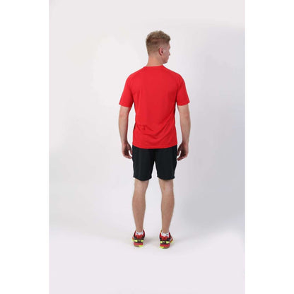 A person stands with their back to the camera, showcasing a comfortable FZ Forza Balkan Red Boys/Mens Badminton T-Shirt, paired with black shorts and red sports shoes featuring vibrant yellow accents, all set against a plain white background.